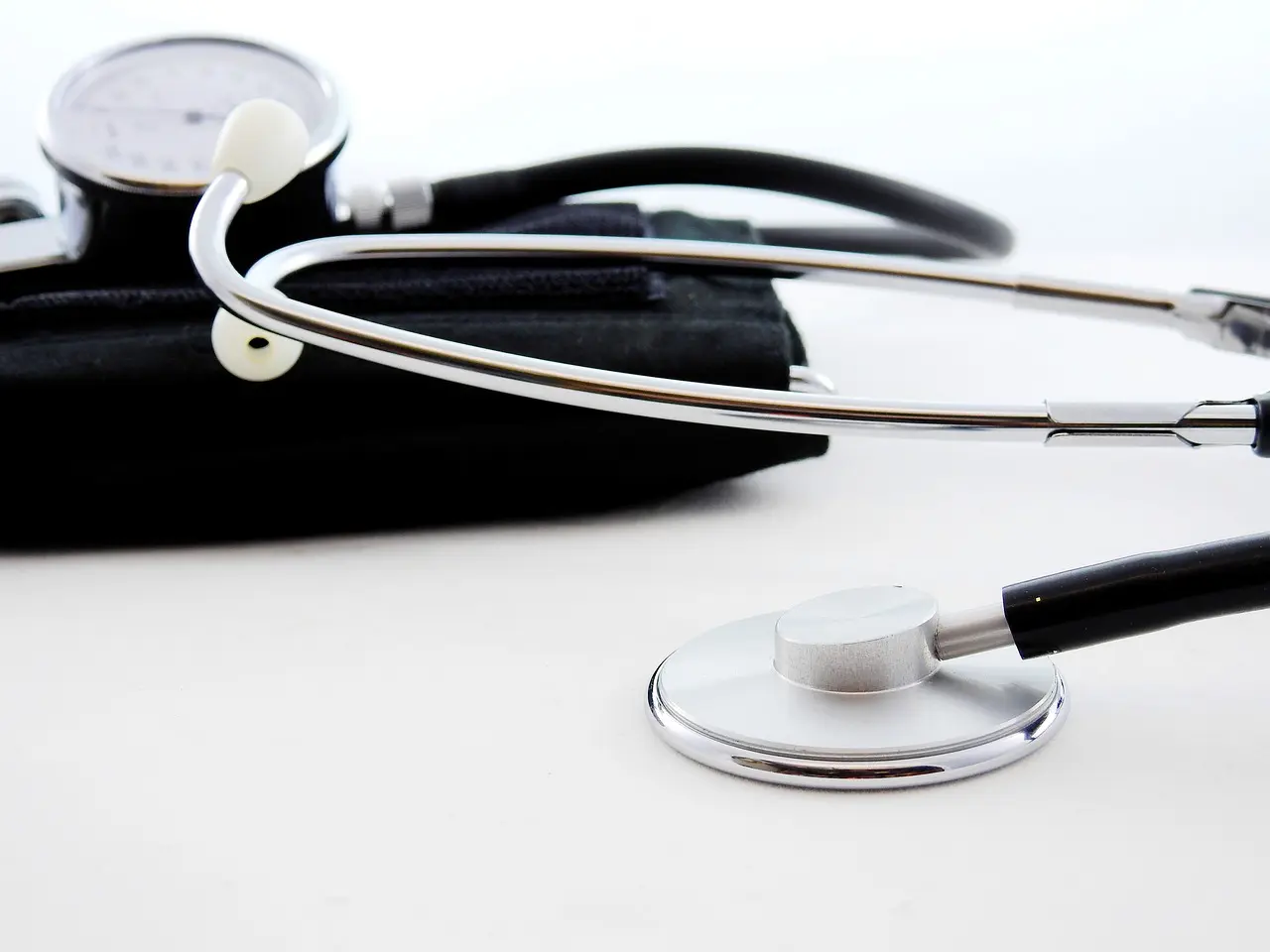 A stethoscope and a blood pressure cuff are placed on a white surface,