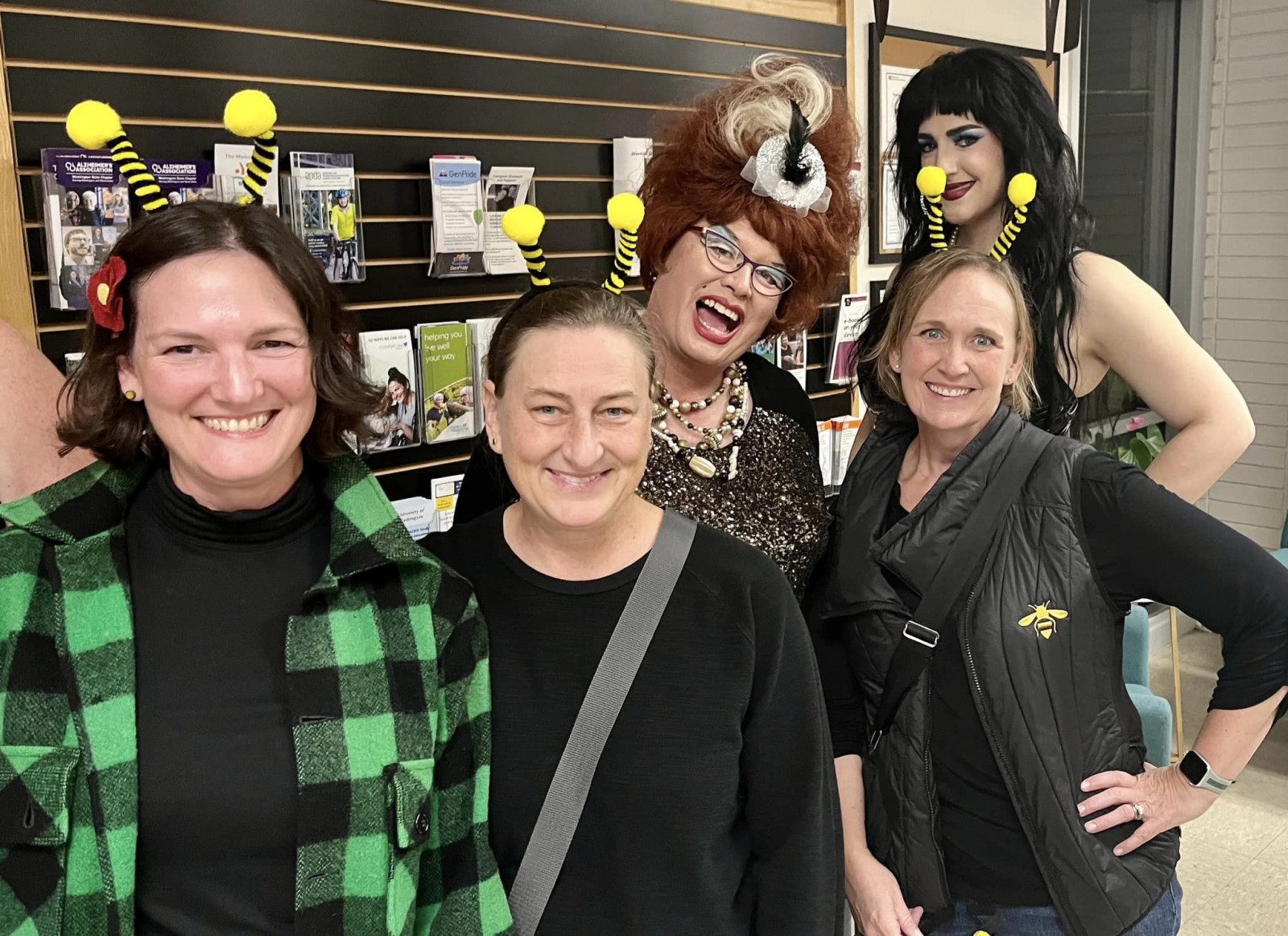 A group of five people wearing bee antenna headbands are smiling. They are standing in front of a display of brochures and books about activities for seniors in West Seattle.