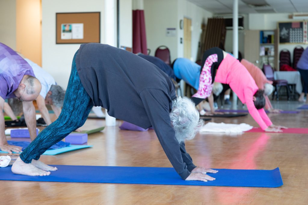 A group of people practice yoga indoors, performing the downward dog pose on yoga mats.