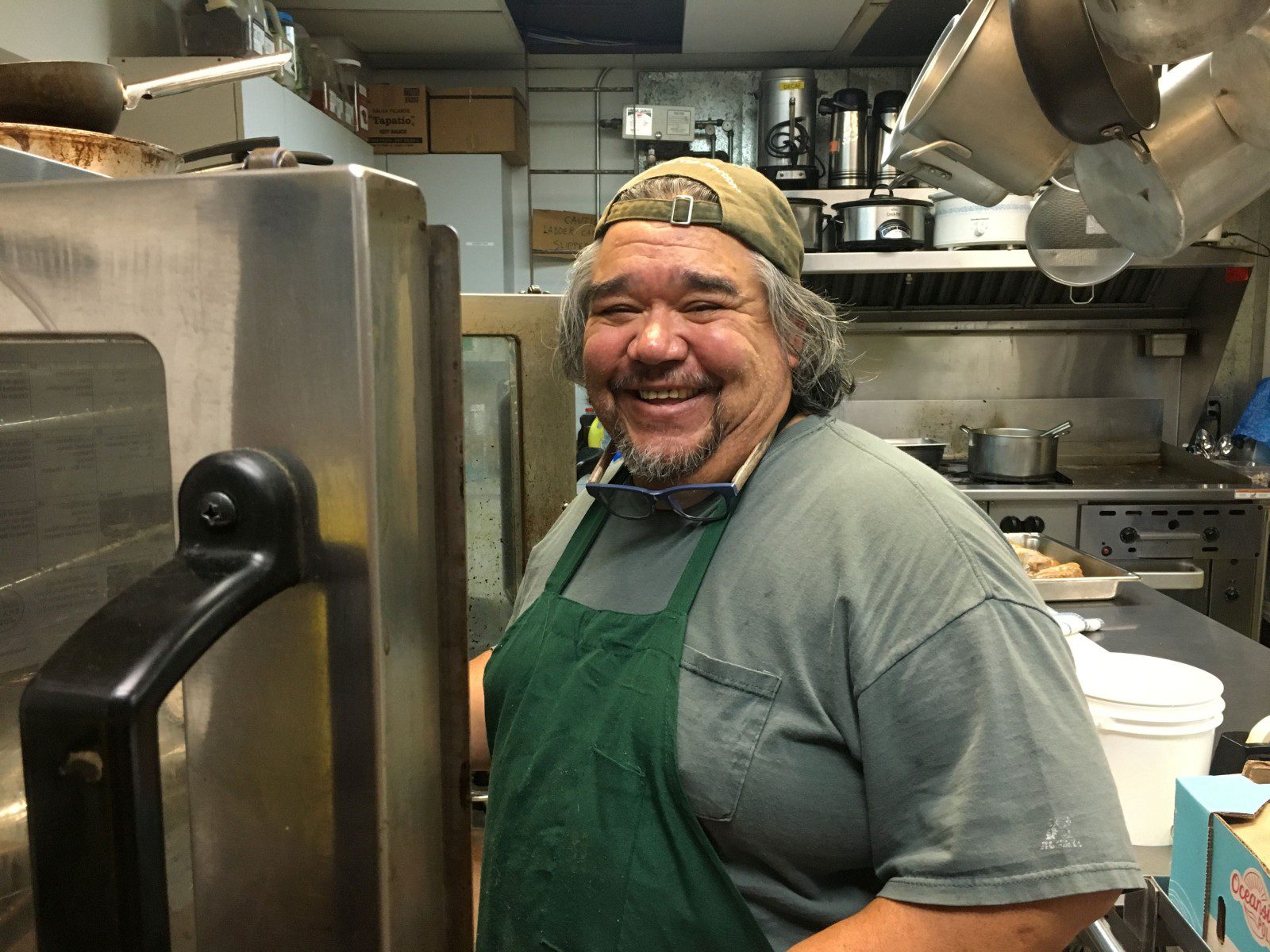 Chef Francisco wearing a green apron and tan cap smiles while in the Center's kitchen