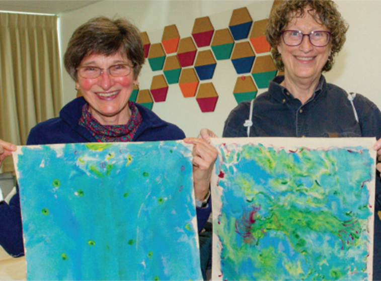 Two people smiling and proudly holding up their vibrant fabric painting creations, each piece a testament to the beauty of abstract art.