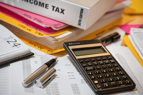 A calculator, pens, and documents are spread across a table