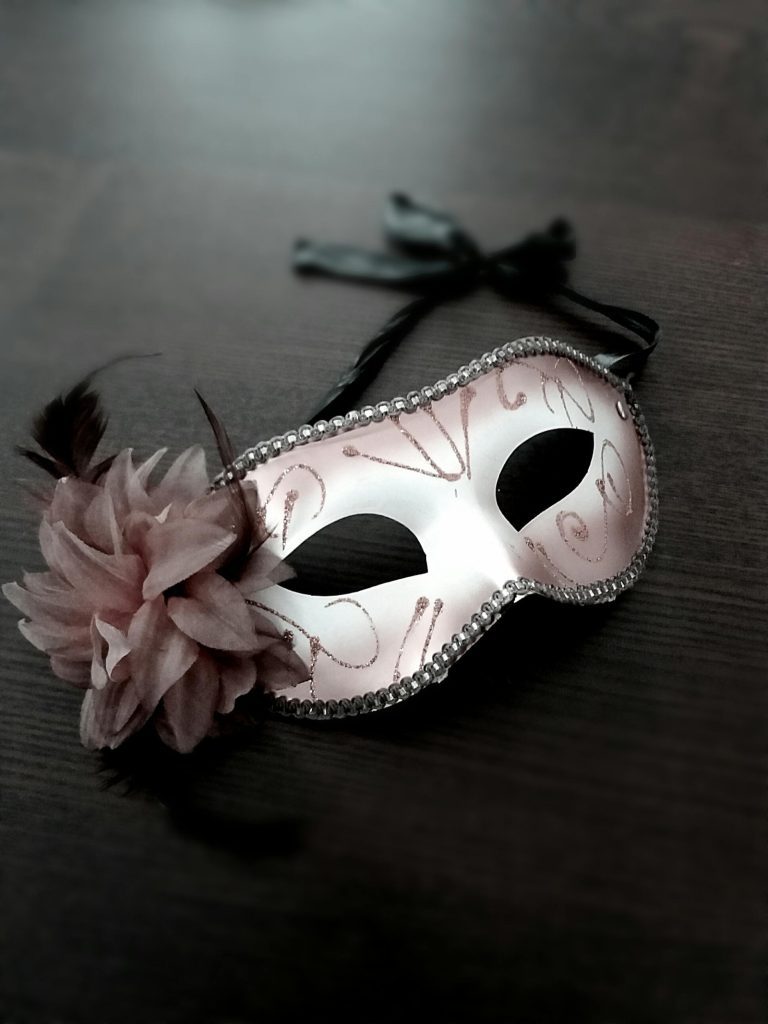 A decorative masquerade mask with pink and gold designs, black ribbons