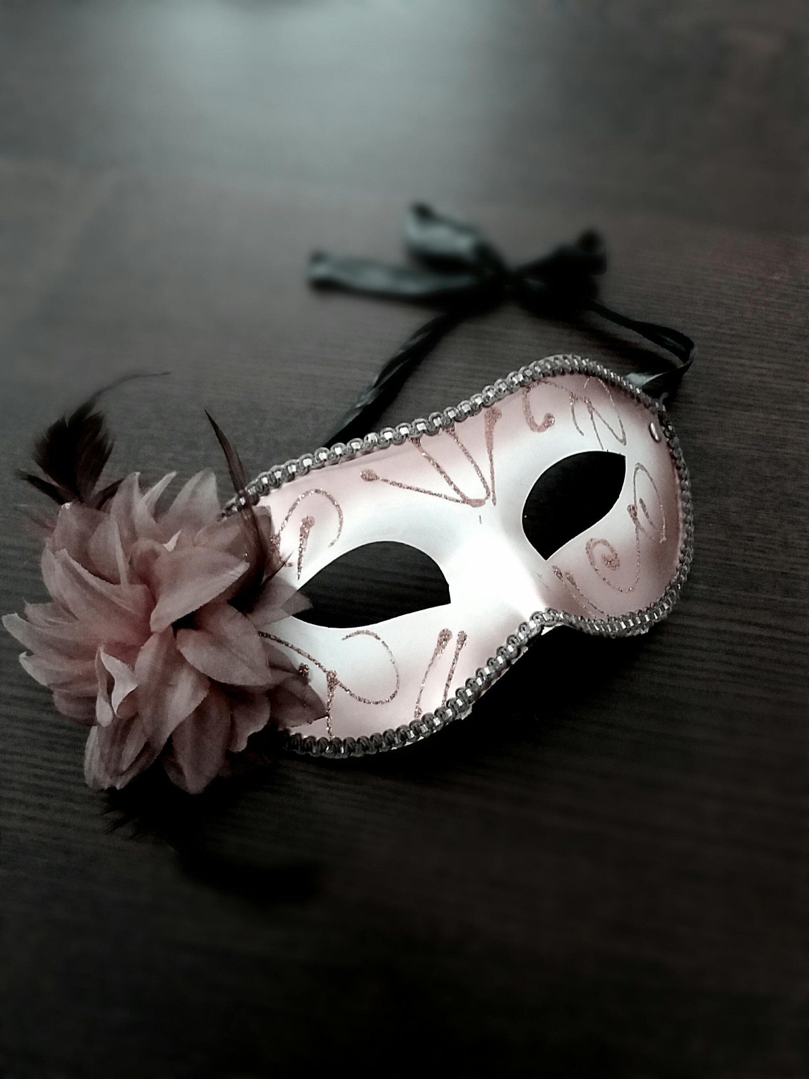 A decorative masquerade mask with pink and gold designs, black ribbons
