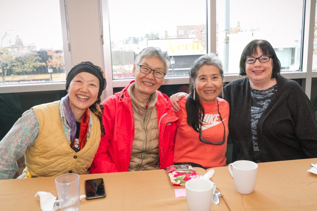 Four women sit side by side at a table, smiling at the camera