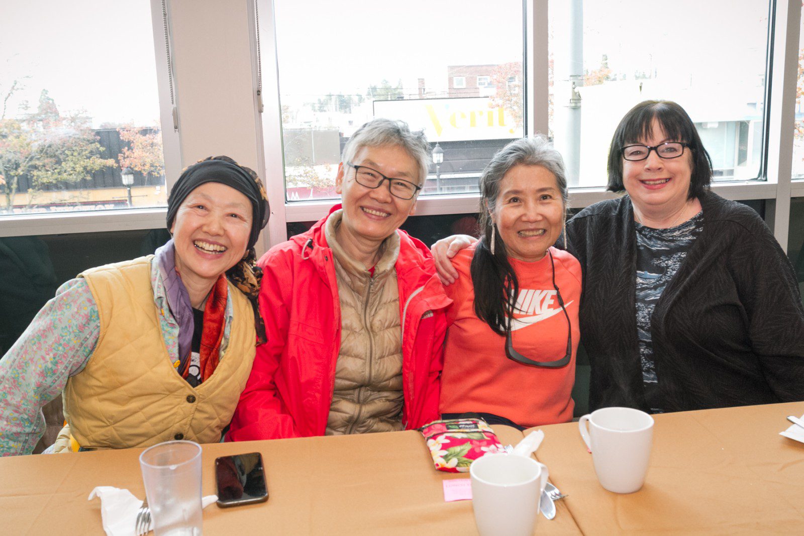 Four women sit side by side at a table, smiling at the camera