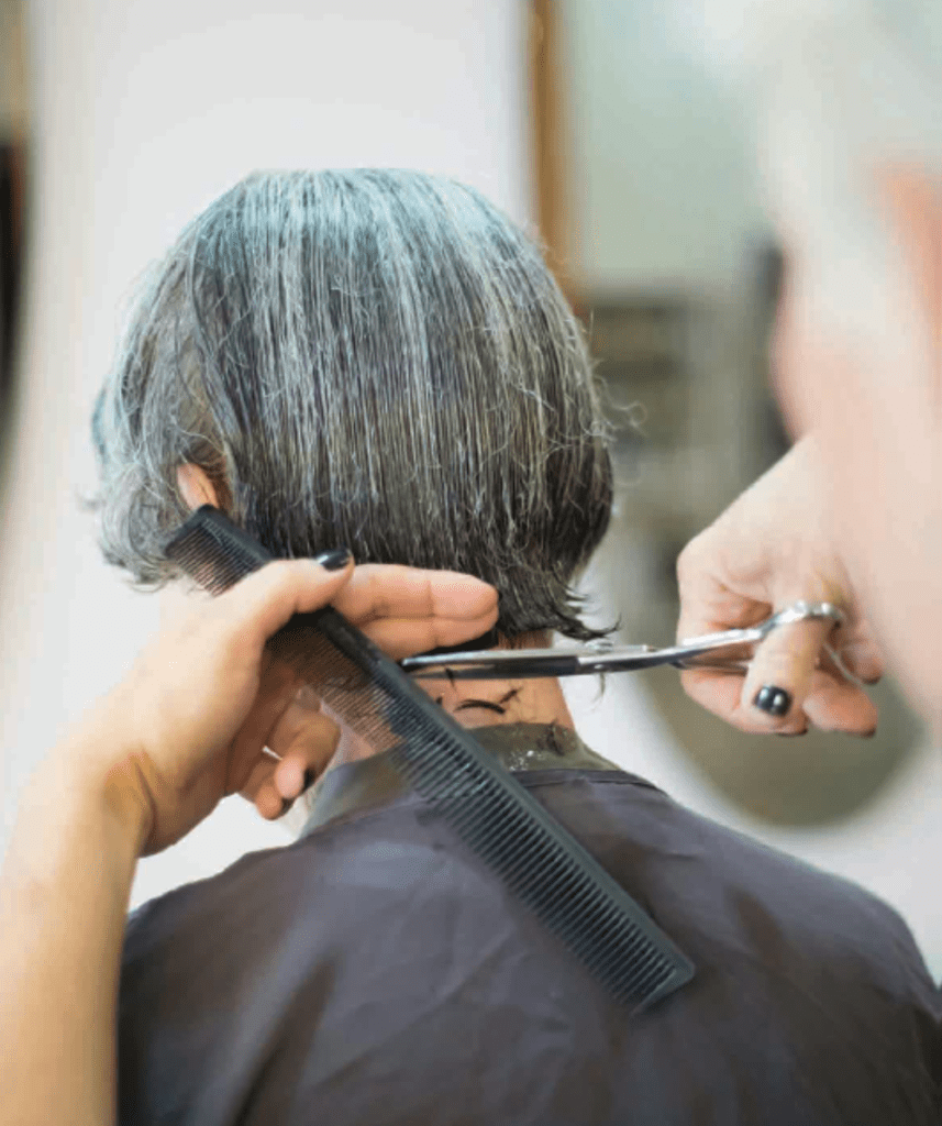 A person with short gray hair is getting a hair cut