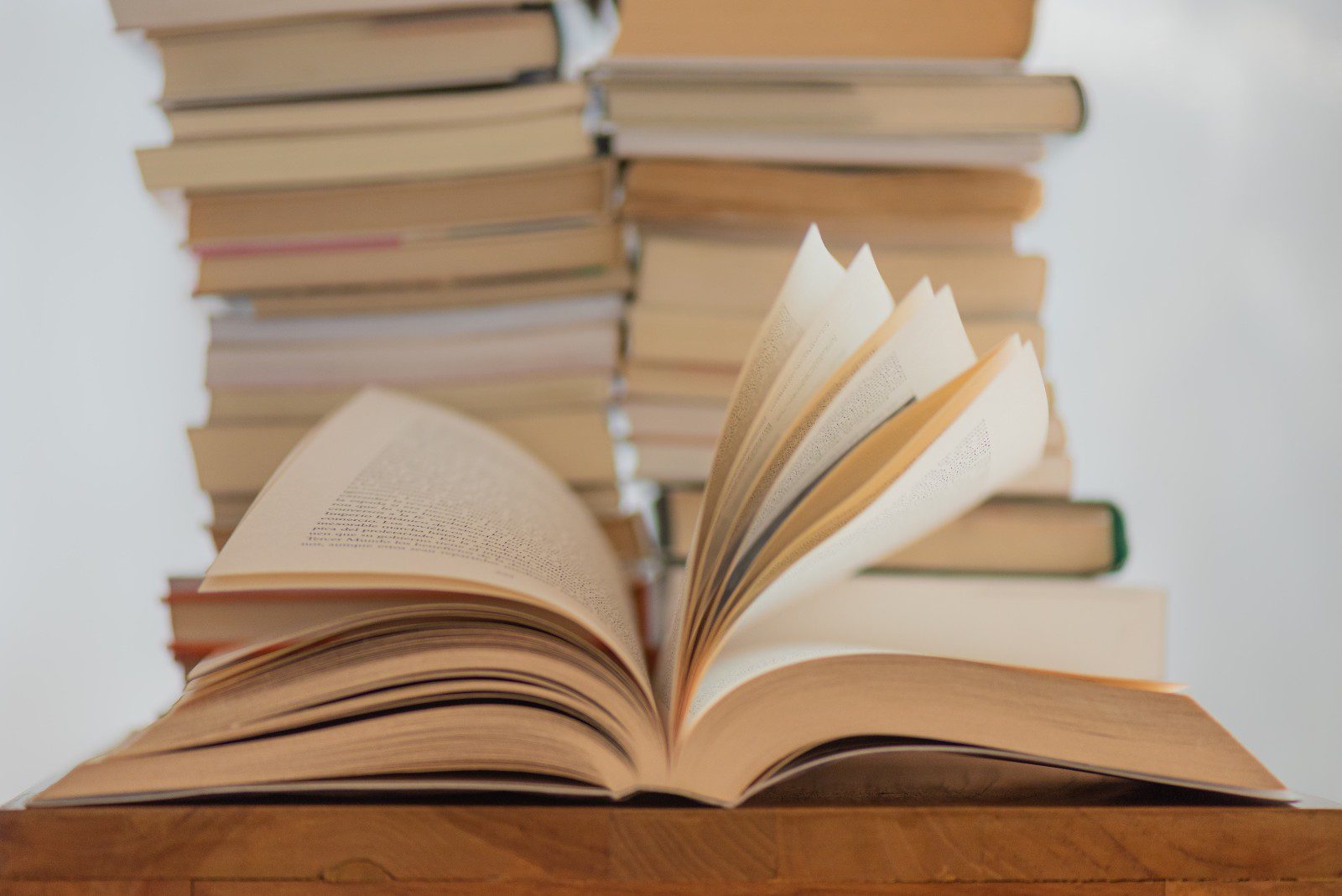 An open book sits at The Center of a wooden surface, inviting quiet reading, while stacks of closed books rest in the background.