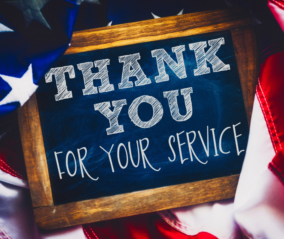A chalkboard sign reading “THANK YOU FOR YOUR SERVICE” is surrounded by an American flag, honoring veterans