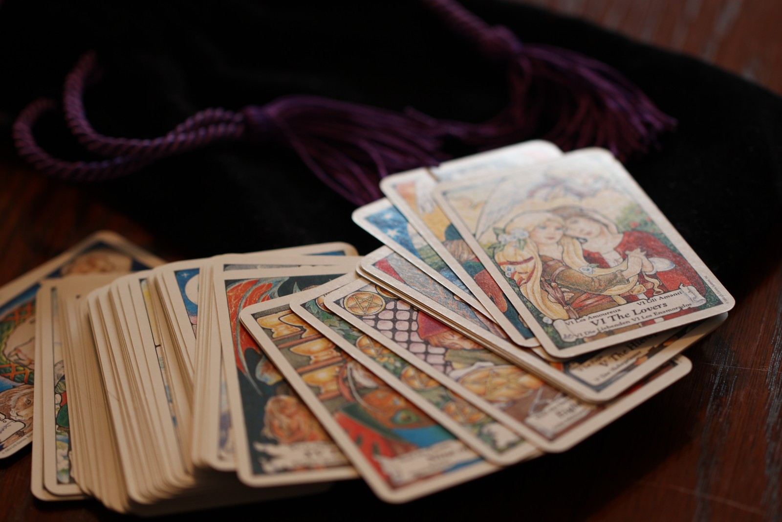 A spread of colorful tarot cards is displayed on a wooden surface next to a black pouch with purple drawstrings