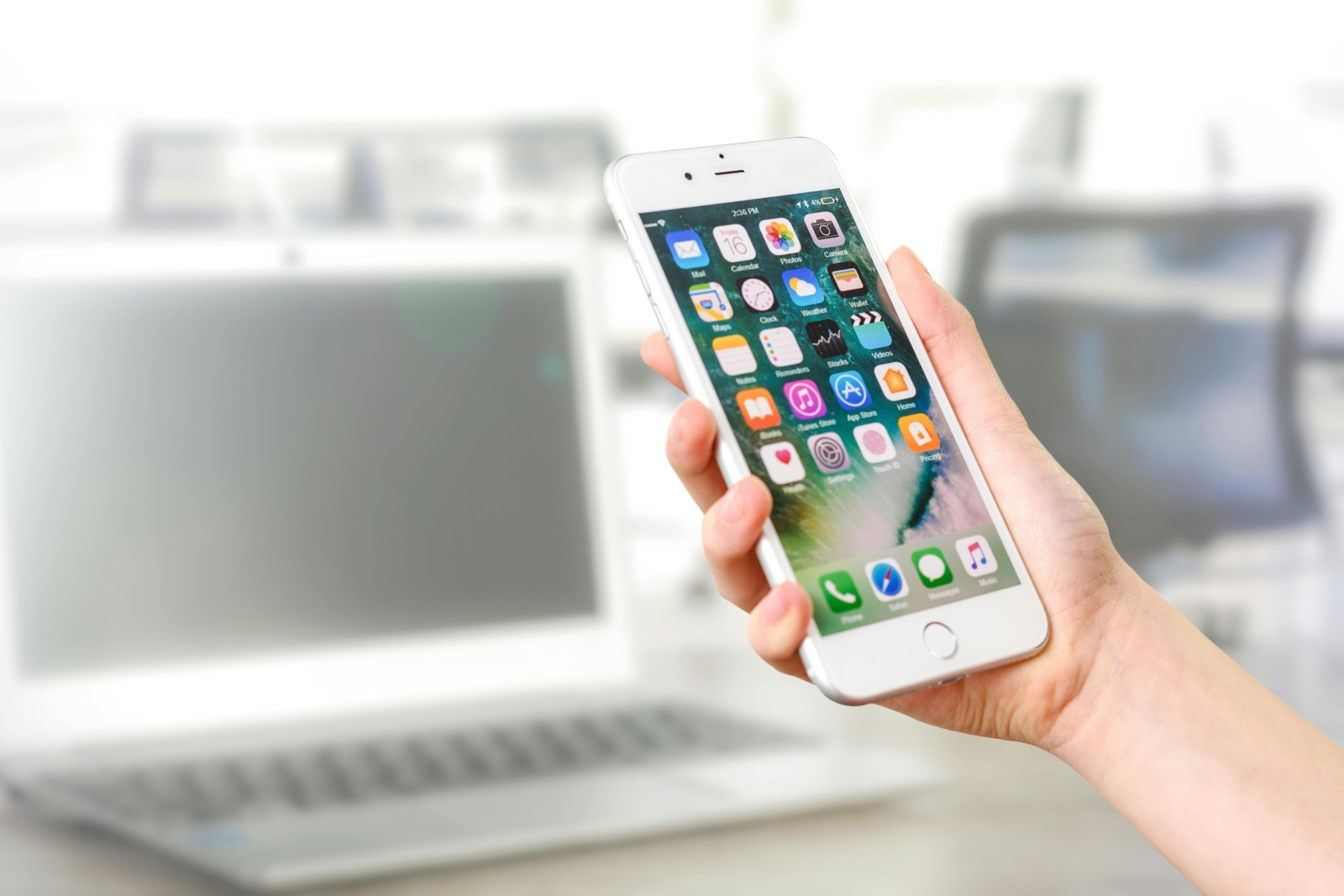 A person holds a smartphone with the home screen visible, displaying various app icons