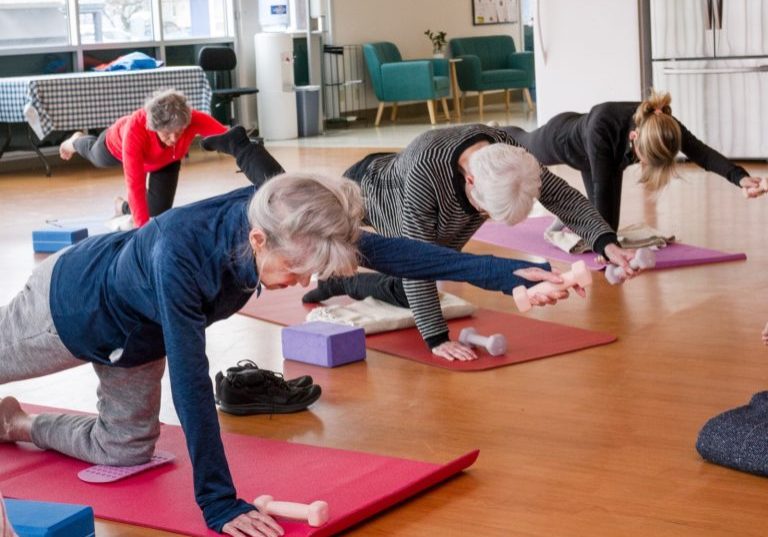Four adults are exercising on yoga mats at The Center