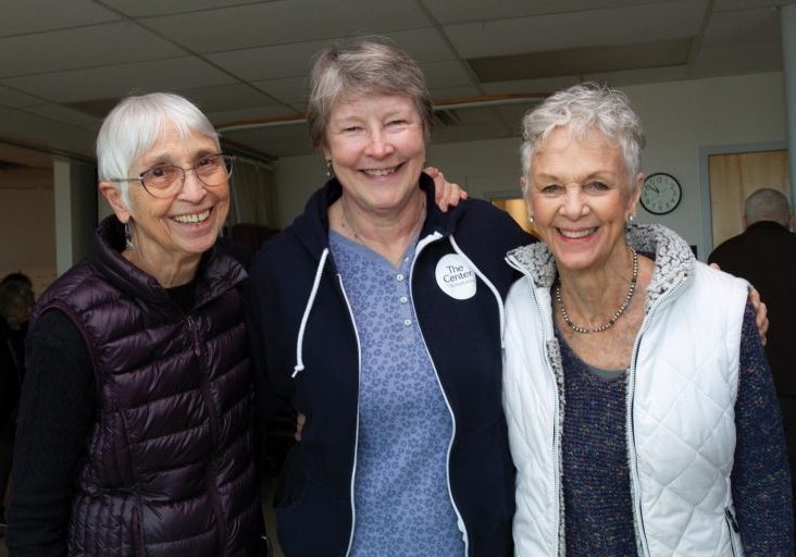 Three women stand together at The Center, smiling at the camera.
