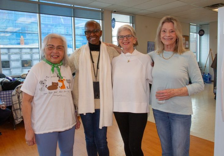 Four women stand together, smiling at the camera with arms around each other.