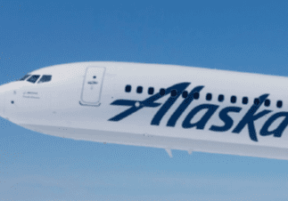 A close-up of the front section of an Alaska Airlines airplane in flight against a clear blue sky