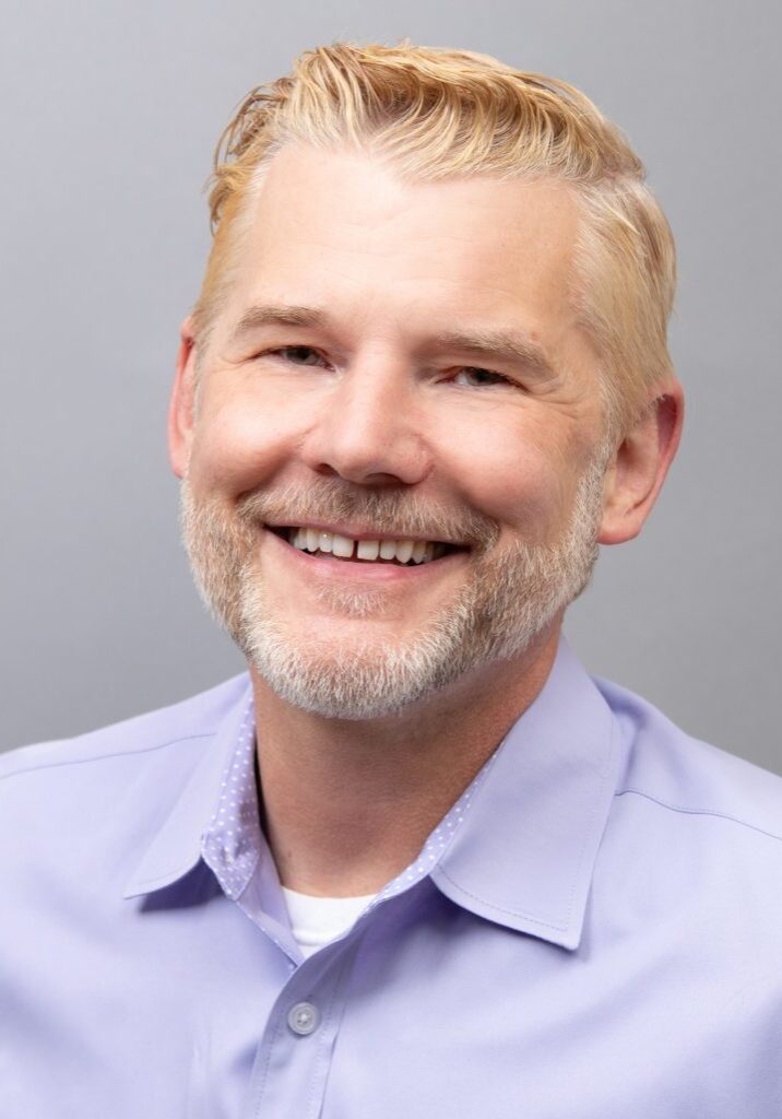 Kevin Ledgerwood, wearing a light purple shirt against a gray background, represents the dedicated team members of the Board at The Center.
