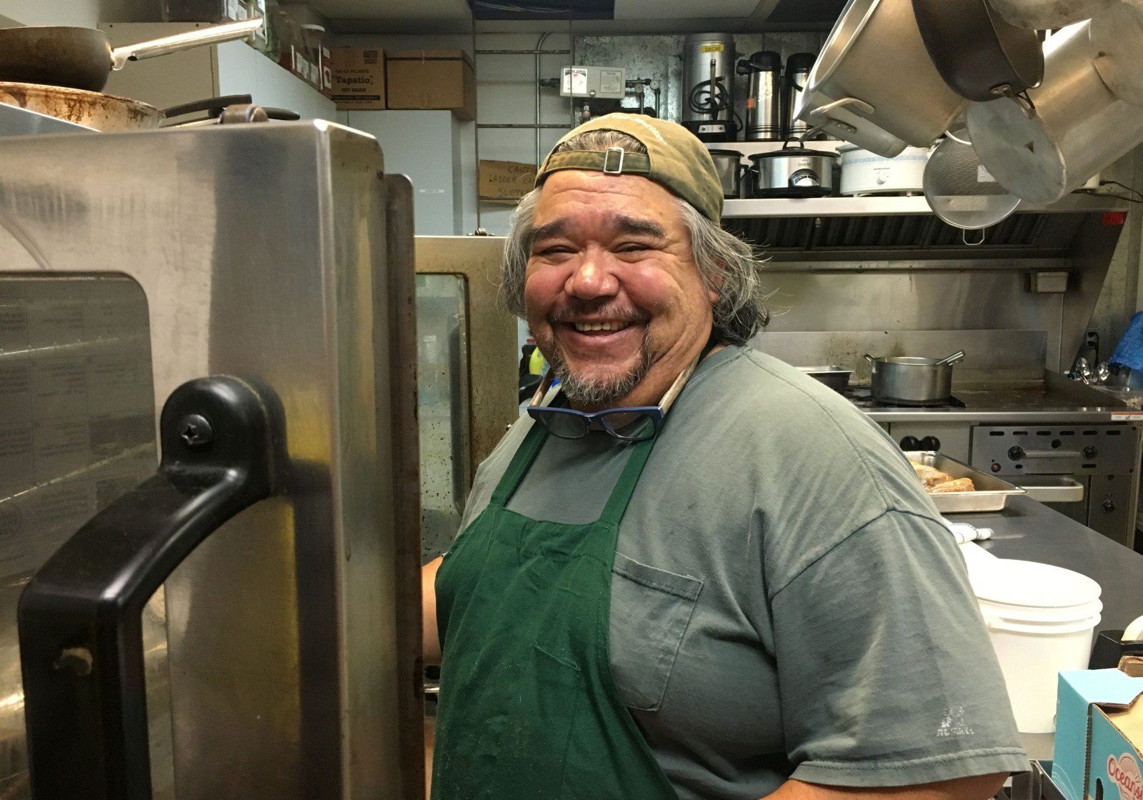 Chef Francisco wearing a green apron and tan cap smiles while in the Center's kitchen