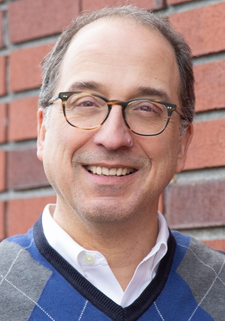 Martin Piccoli smiles in front of a brick wall, representing the Staff at The Center.