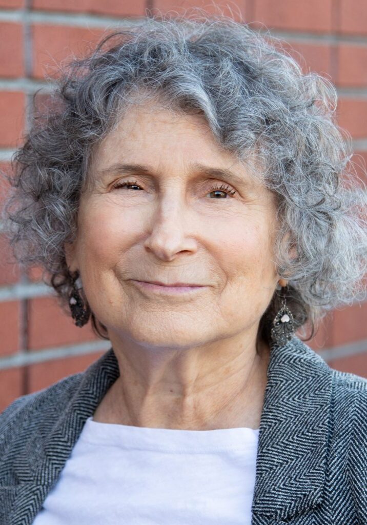 Toni Armeslav stands in front of a brick wall. She is smiling slightly