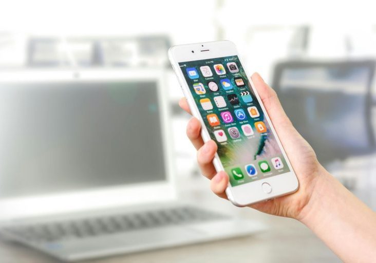 A person holds a smartphone displaying the home screen with app icons